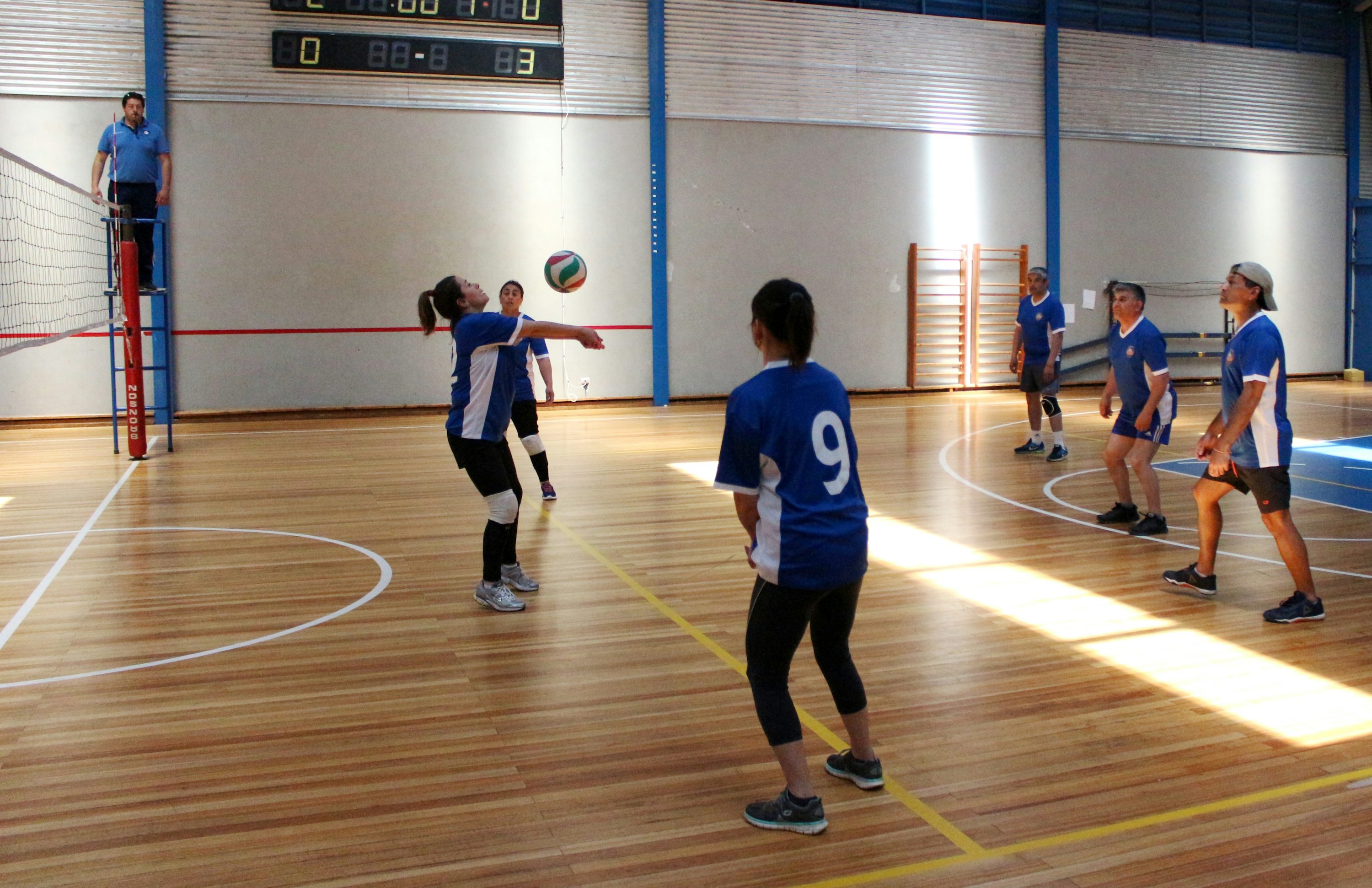 People playing volleyball together on an indoor wooden court.