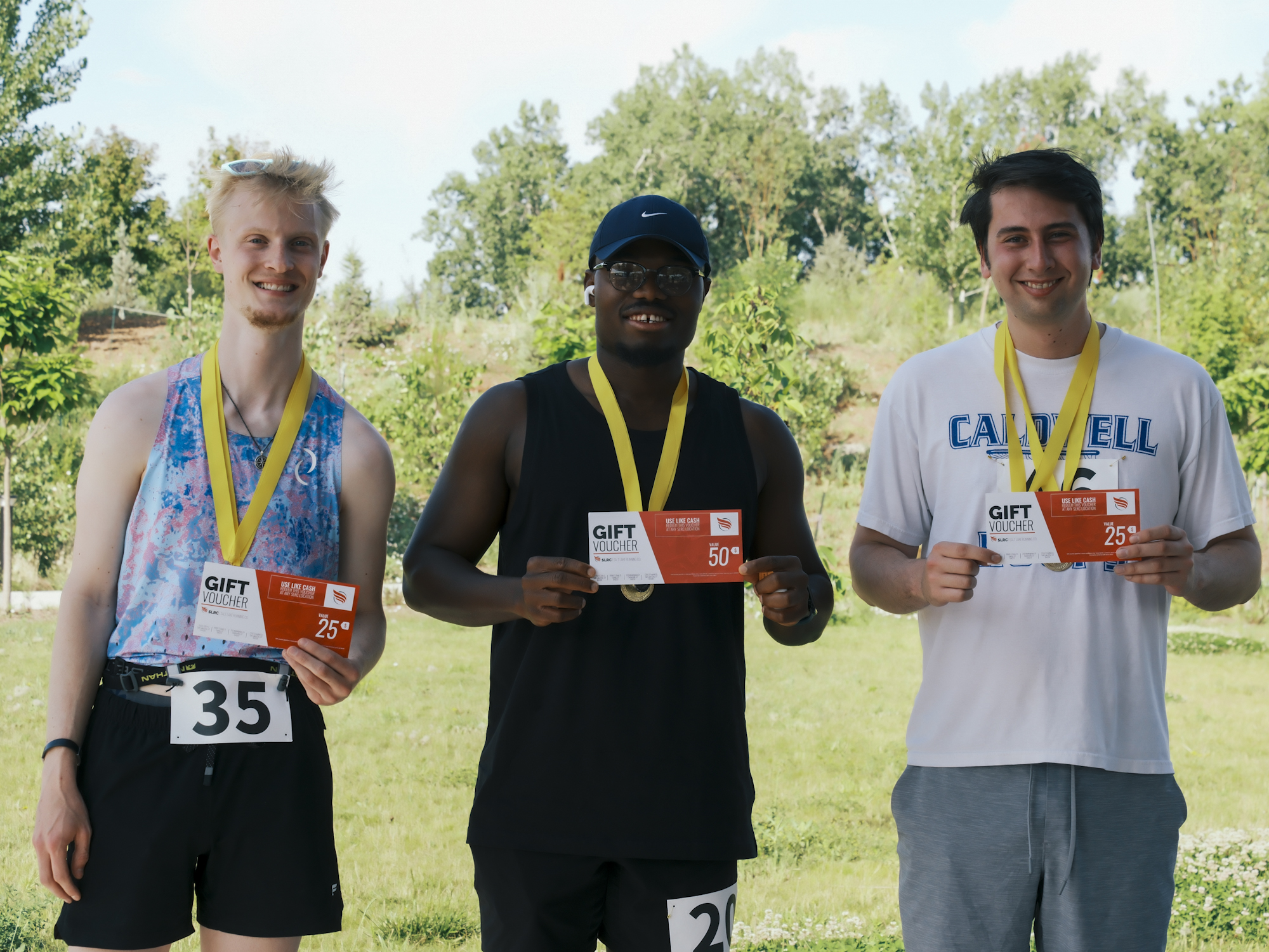 Three finishers smiling with medals and running-store gift vouchers.
